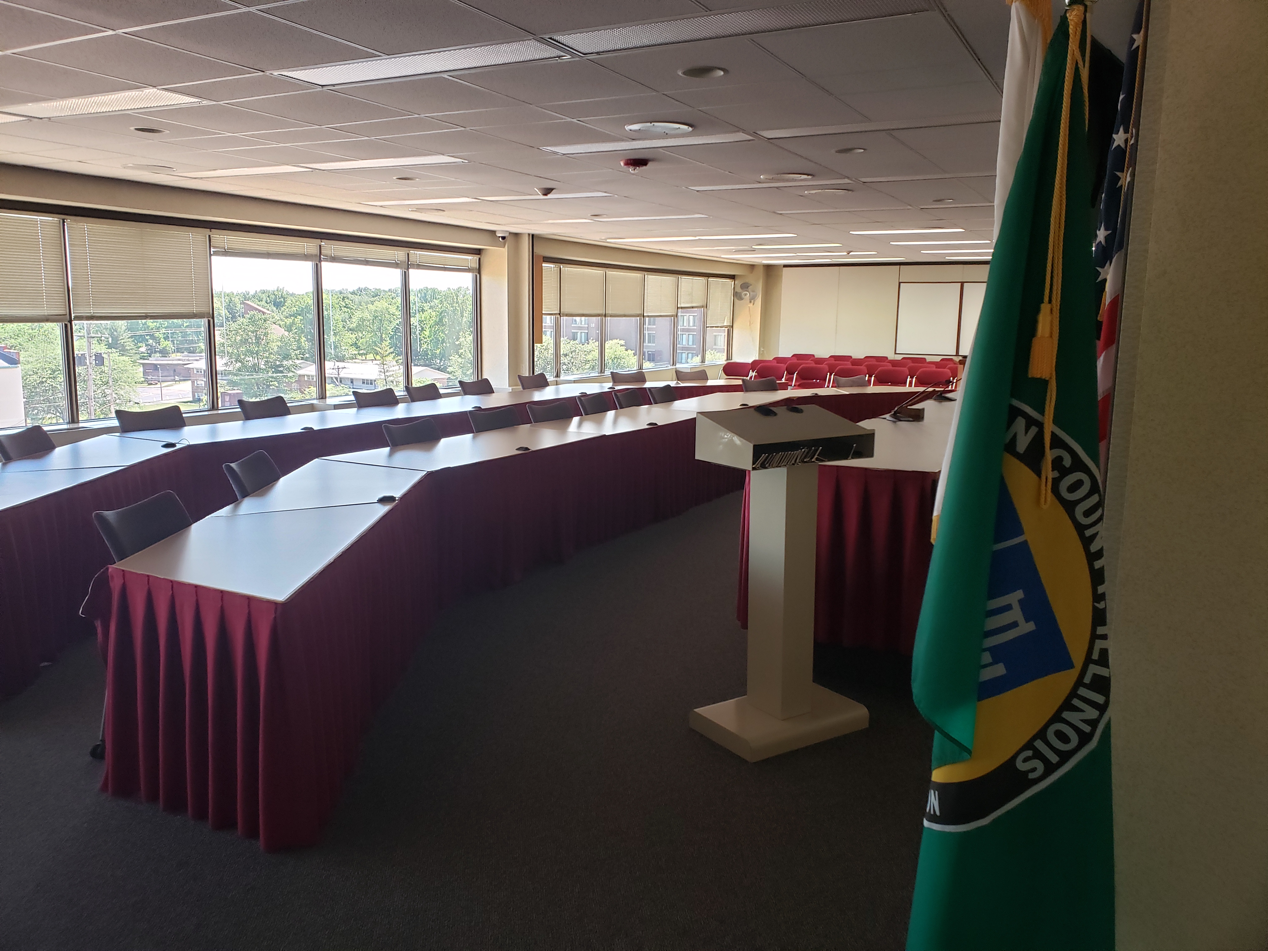 The County Board Room. Two long tables with many chairs. Chairs without tables are in the background.